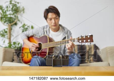 Stock Photo - Japanese man playing guitar at home. Fotosearch