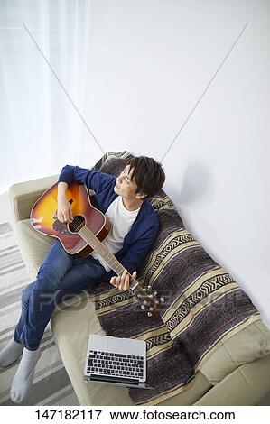 Stock Photo - Japanese man playing guitar at home. Fotosearch