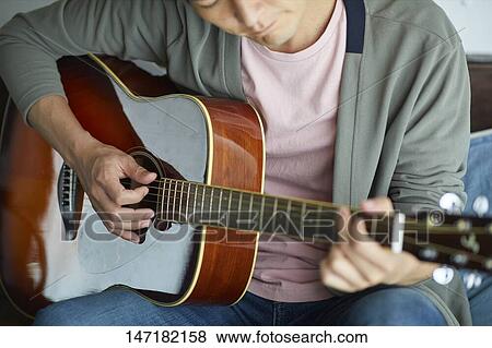 Stock Photo - Japanese man playing guitar at home. Fotosearch