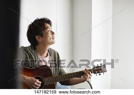 Stock Photo - Japanese man playing guitar at home. Fotosearch