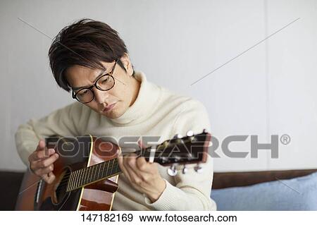 Stock Photo - Japanese man playing guitar at home. Fotosearch