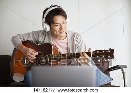 Stock Photo - Japanese man playing guitar at home. Fotosearch