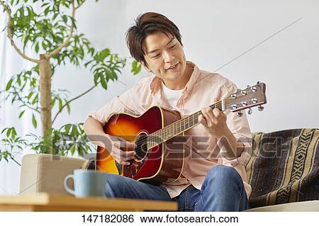 Stock Photograph - Japanese man playing guitar at home. Fotosearch
