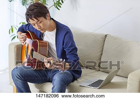 Stock Photograph - Japanese man playing guitar at home. Fotosearch
