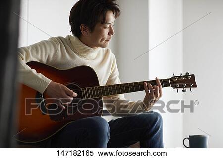 Stock Photography - Japanese man playing guitar at home. Fotosearch