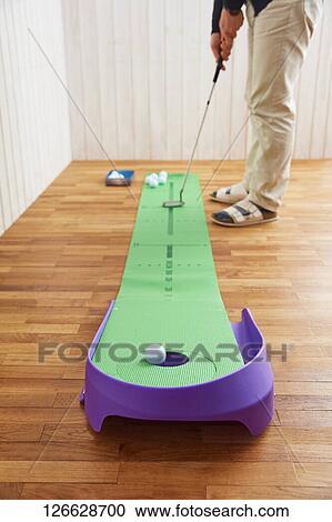Stock Image - Japanese man training for golf at home. Fotosearch