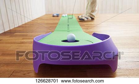 Stock Image - Japanese man training for golf at home. Fotosearch