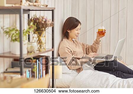 Picture - Japanese woman drinking at home remote drinking. Fotosearch