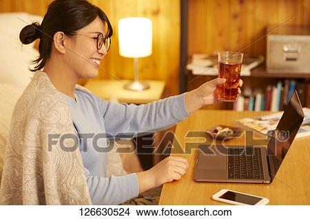 Picture - Japanese woman drinking at home remote drinking. Fotosearch