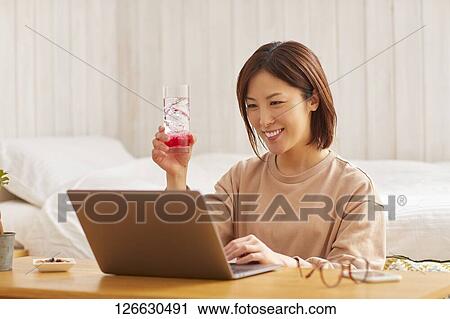 Stock Image - Japanese woman drinking at home remote drinking. Fotosearch
