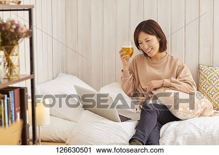 Stock Image - Japanese woman drinking at home remote drinking. Fotosearch