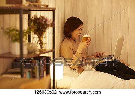 Stock Image - Japanese woman drinking at home remote drinking. Fotosearch