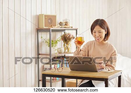 Stock Image - Japanese woman drinking at home remote drinking. Fotosearch