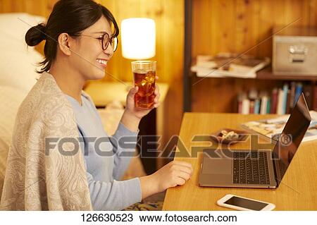 Stock Image - Japanese woman drinking at home remote drinking. Fotosearch