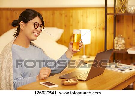 Stock Image - Japanese woman drinking at home remote drinking. Fotosearch