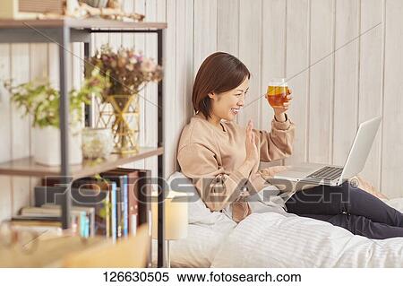 Stock Photography - Japanese woman drinking at home remote drinking. Fotosearch