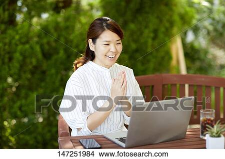 Picture - Japanese woman working with laptop in the garden. Fotosearch