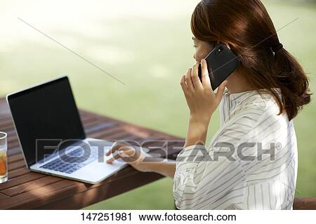 Stock Image - Japanese woman working with laptop in the garden. Fotosearch