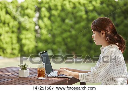 Stock Photo - Japanese woman working with laptop in the garden. Fotosearch
