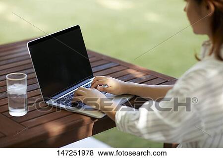 Stock Photo - Japanese woman working with laptop in the garden. Fotosearch