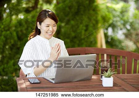 Stock Photography - Japanese woman working with laptop in the garden. Fotosearch