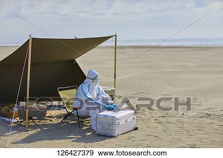 Stock Photo - Man in a hazmat suit at the beach. Fotosearch