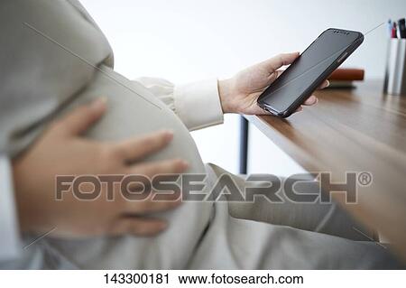 Stock Image - Pregnant Japanese woman with smartphone. Fotosearch
