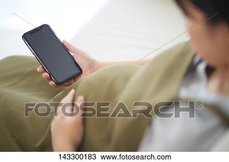 Stock Image - Pregnant Japanese woman with smartphone. Fotosearch