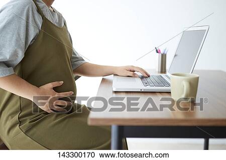 Stock Image - Pregnant Japanese woman working with laptop. Fotosearch
