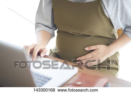 Stock Photo - Pregnant Japanese woman working with laptop. Fotosearch