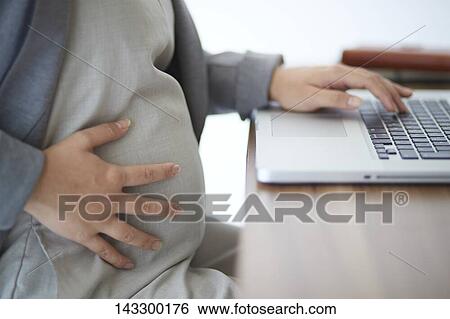 Stock Photograph - Pregnant Japanese woman working with laptop. Fotosearch
