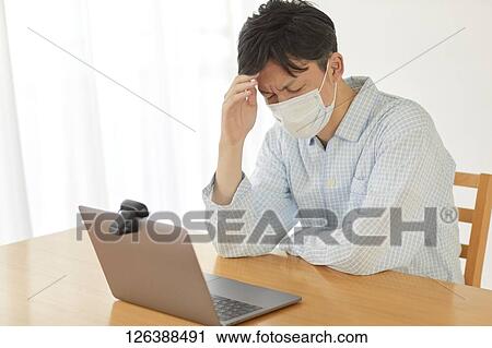 Stock Image - Sick Japanese man working from home. Fotosearch