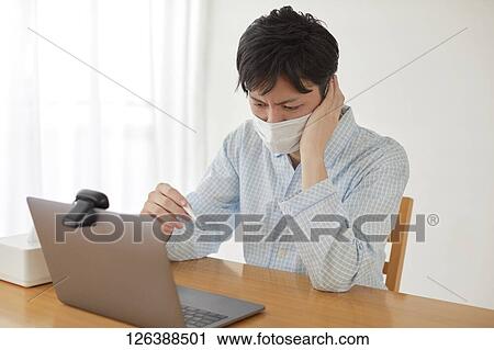 Stock Image - Sick Japanese man working from home. Fotosearch