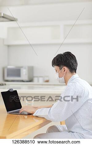 Stock Image - Sick Japanese man working from home. Fotosearch