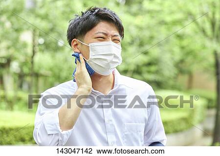 Stock Image - Young Japanese businessman wearing mask in the hot Summer downtown Tokyo. Fotosearch