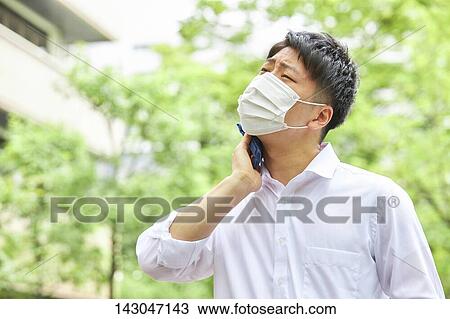 Stock Image - Young Japanese businessman wearing mask in the hot Summer downtown Tokyo. Fotosearch