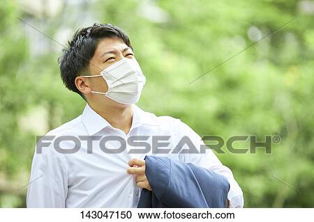 Stock Image - Young Japanese businessman wearing mask in the hot Summer downtown Tokyo. Fotosearch