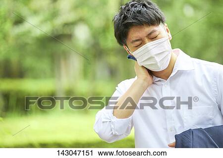 Stock Image - Young Japanese businessman wearing mask in the hot Summer downtown Tokyo. Fotosearch