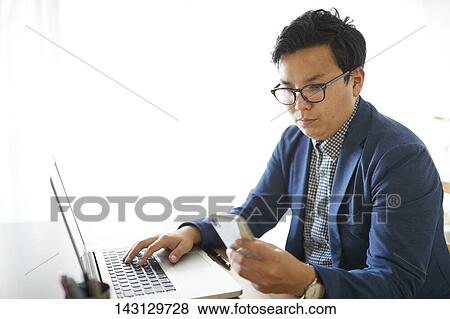 Stock Photo - Young Japanese businessman working with laptop. Fotosearch