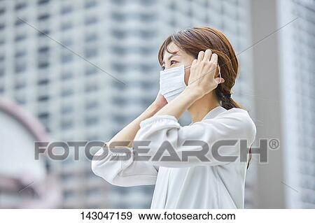 Stock Photo - Young Japanese businesswoman wearing mask in the hot Summer downtown Tokyo. Fotosearch