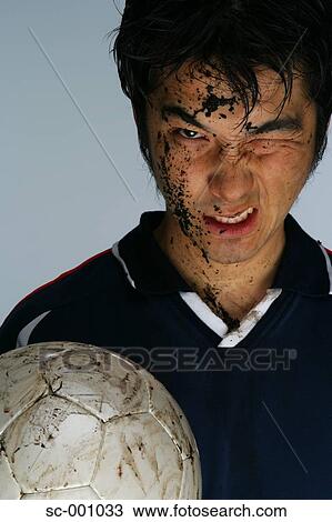 Stock Image - Soccer player grimacing with face covered in mud. Fotosearch