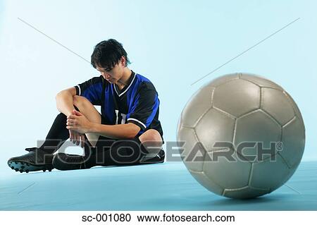 Soccer player sitting with ball in foreground View Large Photo Image Stock Image - Soccer player sitting with ball in foreground. Fotosearch