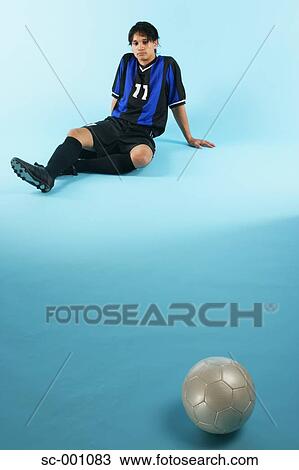 Stock Image - Soccer player sitting with ball in foreground. Fotosearch