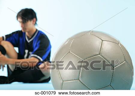 Stock Photo - Soccer player sitting with ball in foreground. Fotosearch