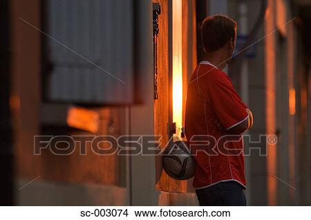 Picture - Man leaning against street wall with ball. Fotosearch