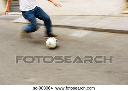 Picture - Man running with soccer ball in street. Fotosearch