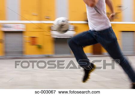 Stock Photo - Man running with soccer ball in street. Fotosearch