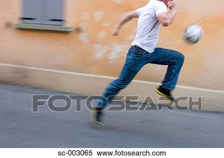 Stock Photography - Man running with soccer ball in street. Fotosearch