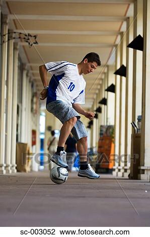 Stock Image - Teenage boy dribbling soccer ball in town. Fotosearch