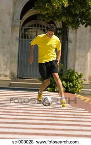 Stock Photo - Teenage boy dribbling soccer ball in town. Fotosearch